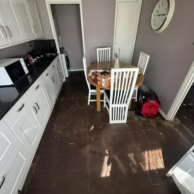 Water covers a kitchen floor beside white cabinets and a small dining table
