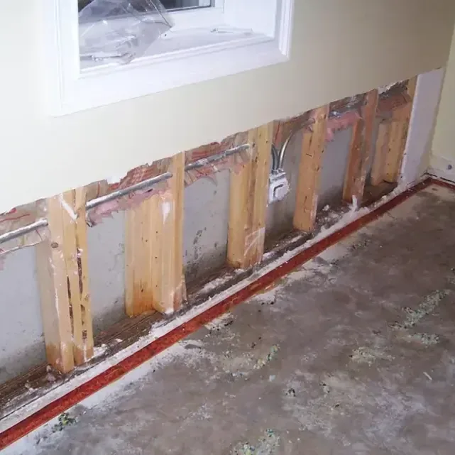 Lower wallboard removed beneath a window, exposing wall studs and a wet floor