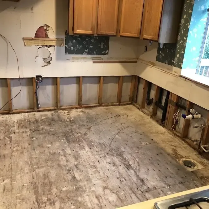 Stripped kitchen flooring and open lower walls reveal framing beneath the remaining upper cabinets