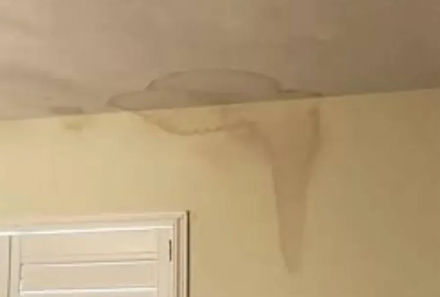 A broad water stain across ceiling plaster and down the adjoining wall