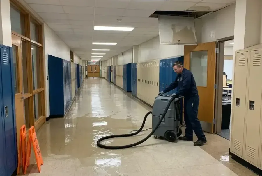 A technician extracting water in a long school corridor lined with blue lockers