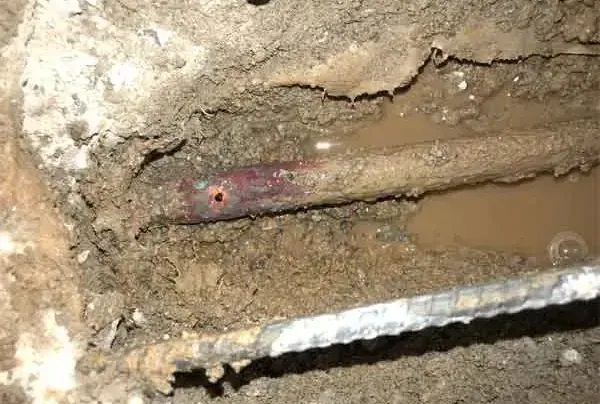 A copper water pipe exposed in wet soil beneath an opened concrete slab