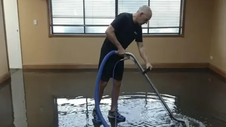 A technician extracting standing water from the floor of an emptied room